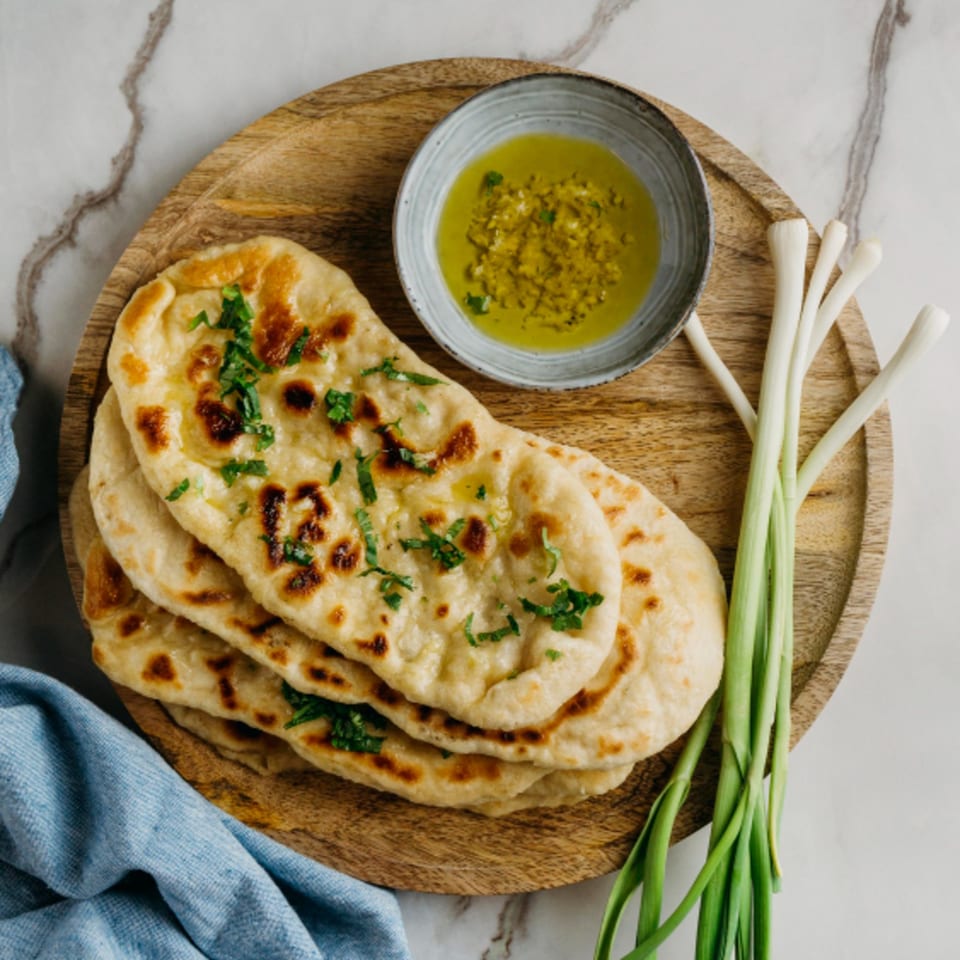 Indian naan bread with cilantro, a bowl of green sauce, and green onions on a wooden tray.