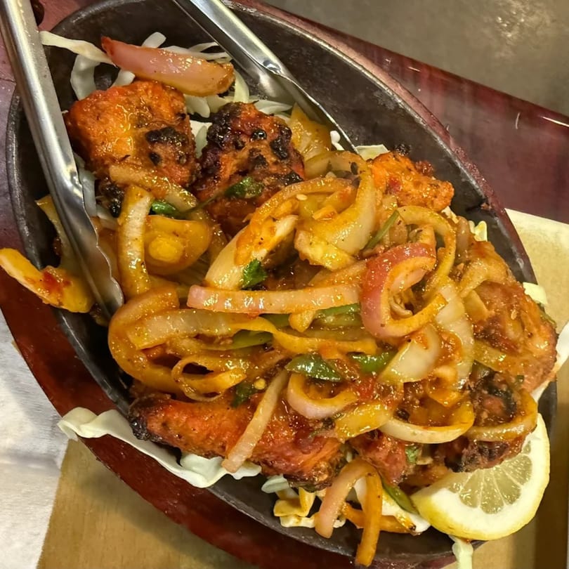 Sizzling Indian chicken tikka with onions, peppers, and a lemon wedge in a hot skillet.