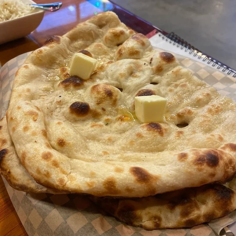 Freshly baked Indian naan bread with melting butter, served with a side of rice.